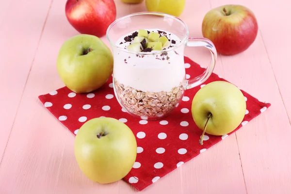 Oatmeal with yogurt in pitcher and apples on napkin on wooden background — Stock Photo, Image