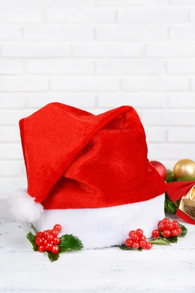 Leaves of mistletoe with Christmas hat on table on brick wall background — Stock Photo, Image