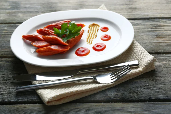 Smoked thin sausages and vegetables on plate, on wooden background — Stock Photo, Image