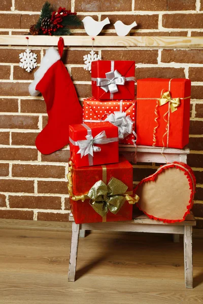 Рождественские подарки на белом стуле на фоне коричневой кирпичной стены — стоковое фото