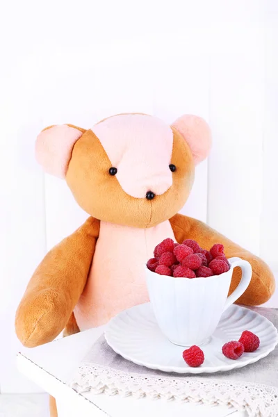 Toy bear and cup of raspberries on wooden wall background — Stock Photo, Image