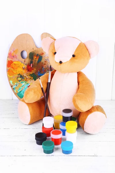Brinquedo urso, paleta e tintas no fundo da parede de madeira — Fotografia de Stock
