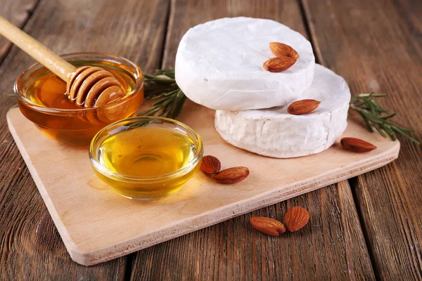 Camembert cheese, honey in glass bowl on cutting board on wooden background — Stock Photo, Image