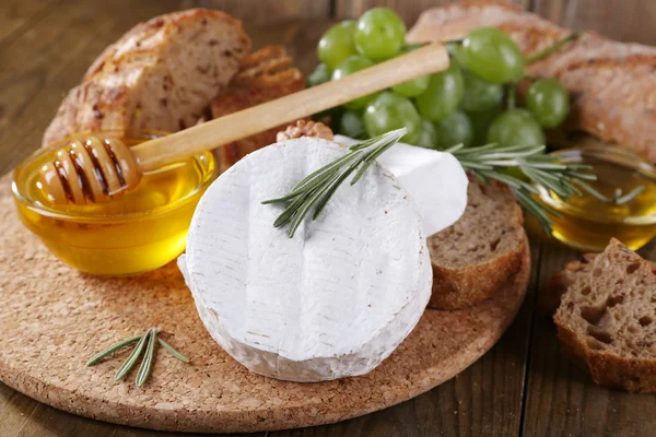 Camembert, Brot, Honig und Trauben auf Schneidebrett auf Holzgrund — Stockfoto