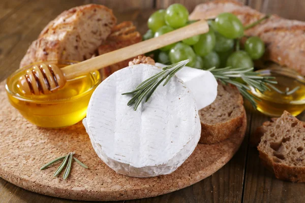 Queijo de camembert, pão, mel e uvas sobre tábua de corte sobre fundo de madeira — Fotografia de Stock