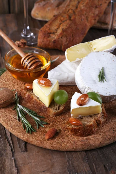 Камамбер сир на папері, винограді, горіхах і меду в скляній мисці на обробній дошці на дерев'яному фоні — стокове фото