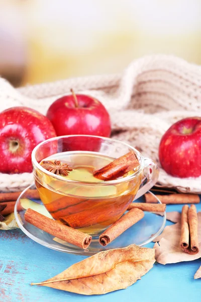 Sammansättningen av äppelcider med kanelstänger, färska röda äpplen, varm halsduk och höstlöv på träbord, på ljus bakgrund — Stockfoto