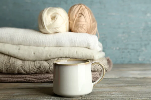 Φλιτζάνι ζεστό ρόφημα, πλέξιμο ρούχα και νήματα σε ξύλινα φόντο — Φωτογραφία Αρχείου