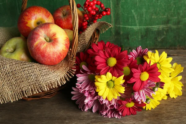 Krásné chryzantémy s jablky v koši na dřevěné pozadí — Stock fotografie
