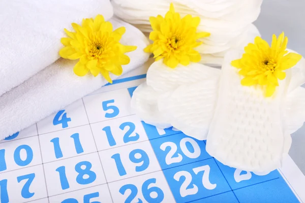 Almofadas sanitárias e flores amarelas no fundo calendário azul — Fotografia de Stock