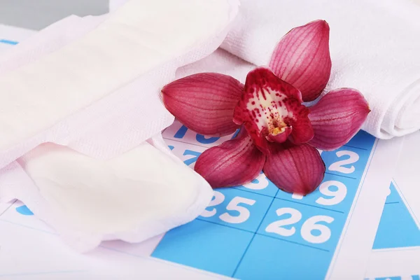 Almofadas sanitárias e orquídea lilás em fundo calendário azul — Fotografia de Stock