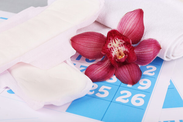 Санитарные прокладки и сиреневая орхидея на фоне голубого календаря
