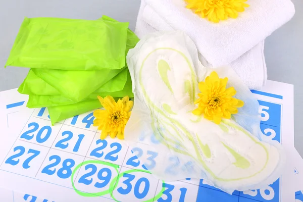 Almofadas sanitárias e flores amarelas no calendário azul no fundo cinza claro — Fotografia de Stock