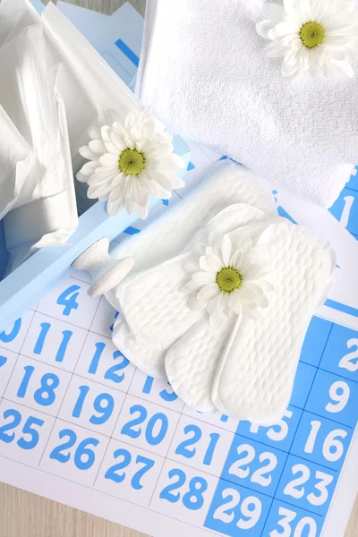 Sanitary pads in box and sanitary pads and white flowers on blue calendar on light grey background — Stock Photo, Image