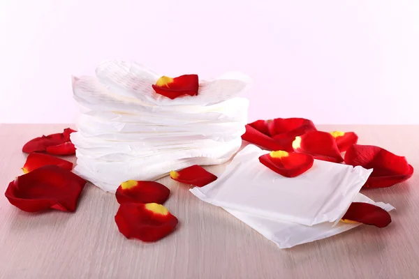 Almofadas sanitárias e pétalas de rosa na mesa de madeira no fundo rosa — Fotografia de Stock