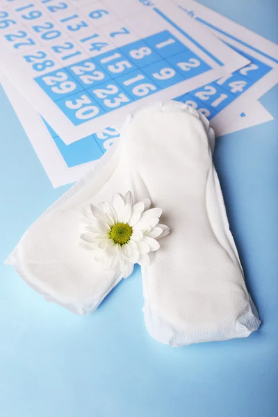 Sanitary pads, calendar and white flower on light blue background — Stock Photo, Image