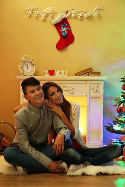 Bonita pareja de amor sentado en la alfombra delante de la chimenea. Mujer y hombre celebrando la Navidad —  Fotos de Stock