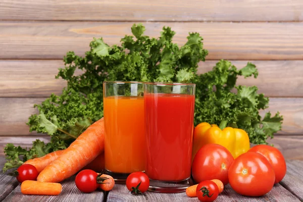 Jus wortel dan tomat dalam gelas dan sayuran segar di meja kayu dengan latar belakang dinding kayu — Stok Foto