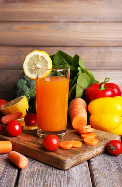 Succo di carota in vetro e verdure fresche su tagliere su tavolo in legno su fondo parete in legno — Foto Stock