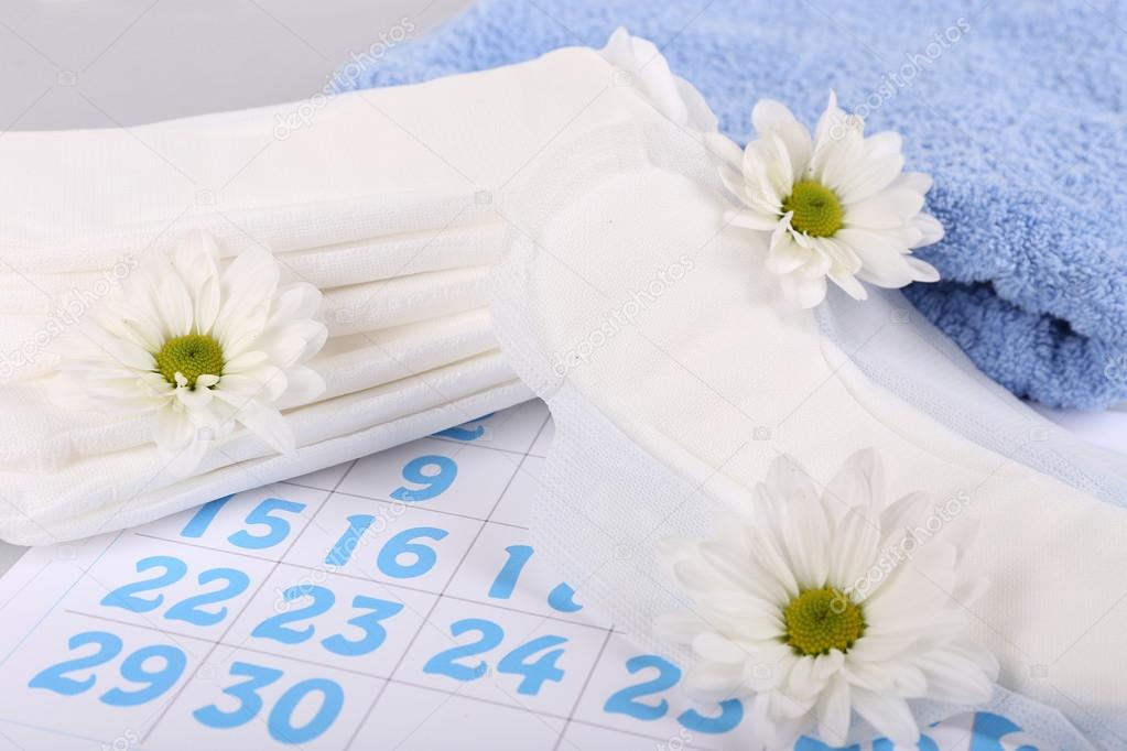 Sanitary pads, calendar, towel and white flowers on light background