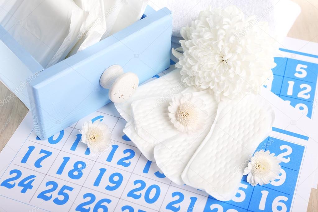 Sanitary pads in box and sanitary pads and white flowers on blue calendar on light grey background