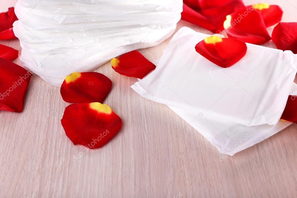 Sanitary pads and rose petals on table on wooden table on pink background