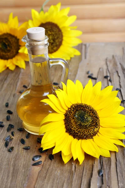 Sunflowers with seeds and oil on wooden background — Stock Photo, Image