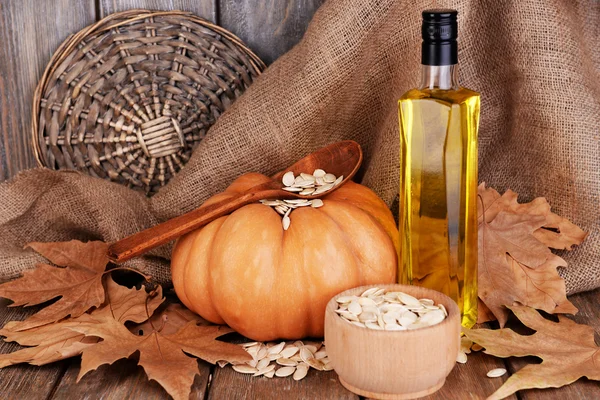 Aceite de semilla de calabaza en botella de vidrio y calabaza fresca sobre fondo de madera — Foto de Stock