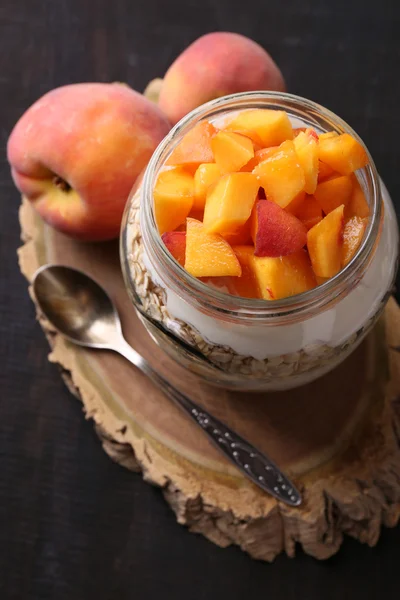 Desayuno saludable yogur con melocotón fresco y muesli servido en frasco de vidrio, sobre fondo de madera — Foto de Stock