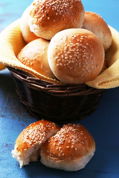 Pães saborosos com gergelim na cesta de vime, na cor de fundo de madeira — Fotografia de Stock