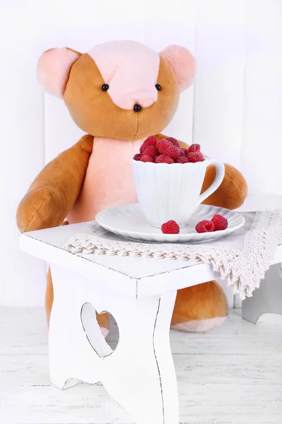 Toy bear and cup of raspberries on wooden wall background — Stock Photo, Image