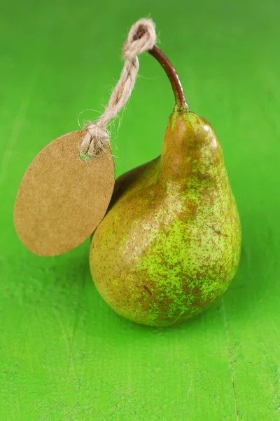 Ripe pear with paper tag on wooden background — Stock Photo, Image