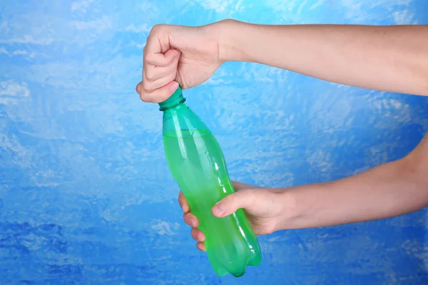 Hand opening bottle with sweet water on blue background — Stock Photo, Image