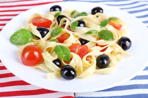 Спагетти с помидорами, оливками и листьями базилика на тарелке на салфетке — стоковое фото