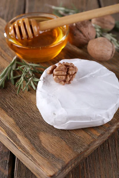 Camembert cheese, honey in glass bowl and nuts on cutting board on wooden background — Stock Photo, Image