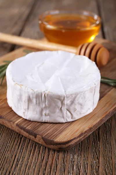 Camembert cheese and honey in glass bowl on cutting board on wooden background — Stock Photo, Image