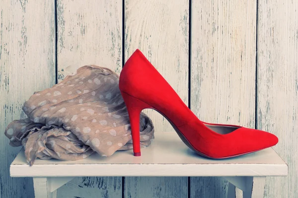 Czerwone damskie buty i szalik na ławce na drewnianym tle — Zdjęcie stockowe