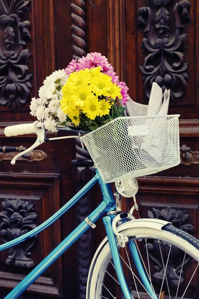 Vecchia bicicletta con fiori in cesto di metallo su sfondo porta marrone — Foto Stock