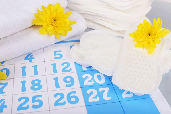 Almofadas sanitárias e flores amarelas no fundo calendário azul — Fotografia de Stock