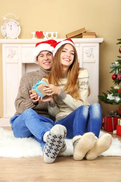 Young couple with gifts, sitting on carpet, at home — Stock Photo, Image