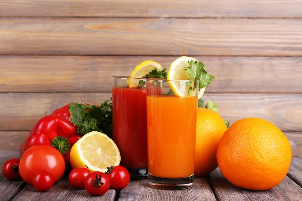 Karotten- und Tomatensaft in Gläsern und frischem Gemüse auf Holztisch vor Holzwandhintergrund — Stockfoto