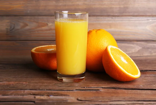 Vaso de zumo de naranja y naranjas frescas sobre mesa de madera sobre fondo de pared de madera — Foto de Stock