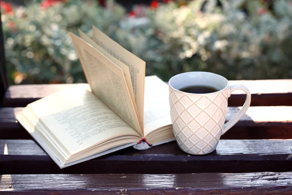 Cup with hot drink and book on bench, outdoors — Stock Photo, Image
