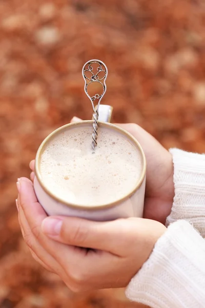 Frau hält Tasse mit leckerem Heißgetränk, Nahaufnahme, auf Herbstblättern Hintergrund — Stockfoto