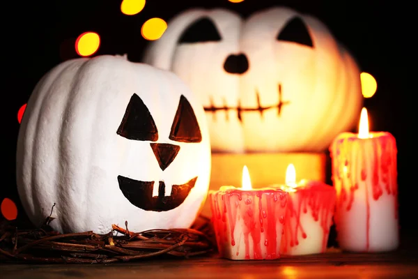 Calabazas y velas blancas de Halloween en la mesa sobre fondo de color oscuro con luces multicolor — Foto de Stock