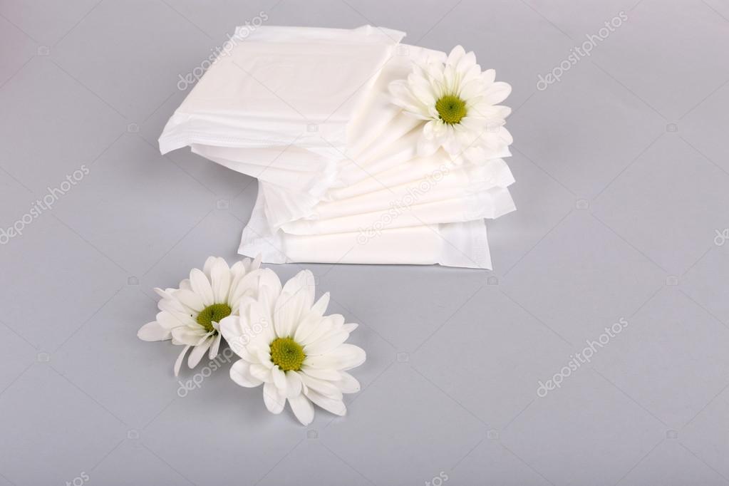 Sanitary pads and white flowers on light background