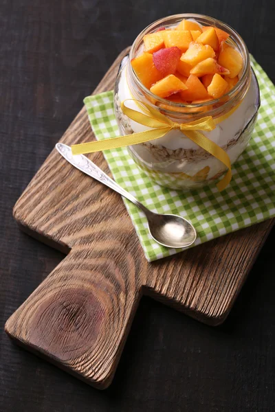 Petit déjeuner sain - yaourt aux pêches fraîches et muesli servi dans un bocal en verre, sur fond de bois — Photo