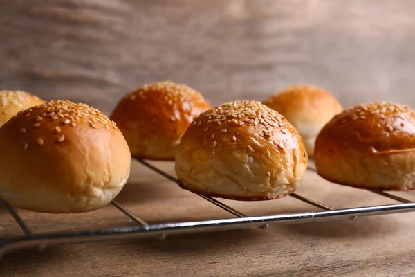 Tasty buns with sesame on oven-tray, on wooden background — Stock Photo, Image