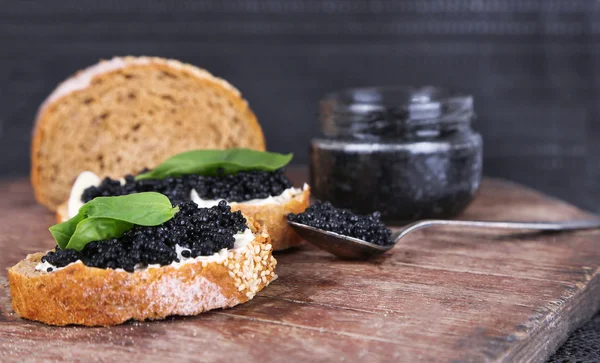 Rebanadas de pan con mantequilla y caviar negro sobre mesa de madera sobre fondo oscuro — Foto de Stock