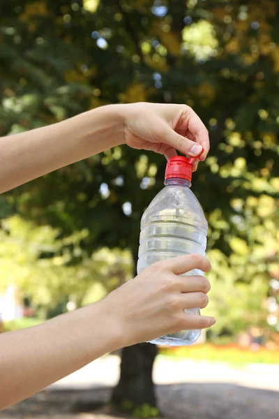 Hand opening bottle with water on bright background — Stock Photo, Image